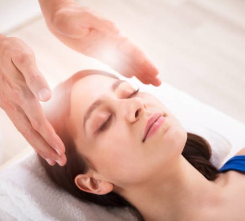 Close-up Of Therapist's Hand Performing Reiki Treatment On Young Woman In Spa